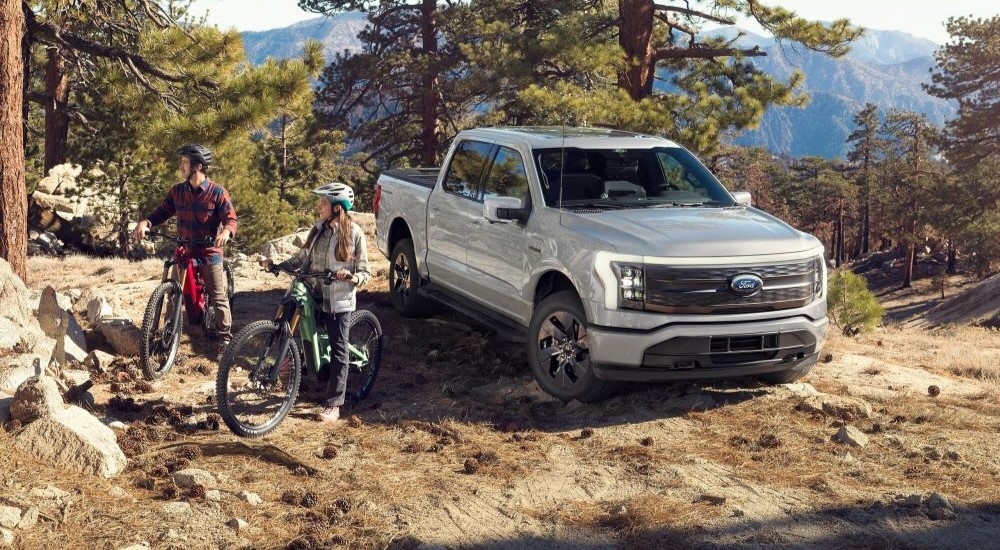 Bikers are shown near a grey 2023 Ford F-150 Lightning for sale near Keene.