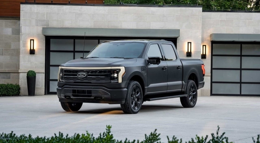 A black 2024 Ford F-150 Lightning for sale near Keene is shown in front of a modern house.