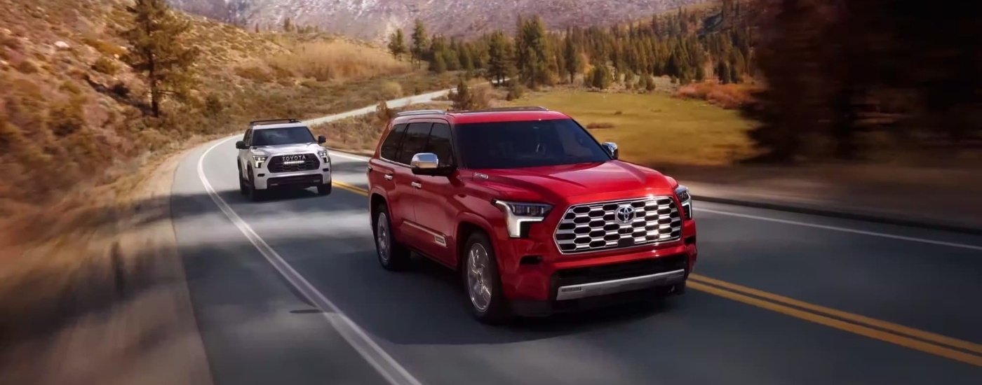 A white 2024 Toyota Sequoia Capstone and red Sequoia TRD Pro are shown on a tree-lined road.