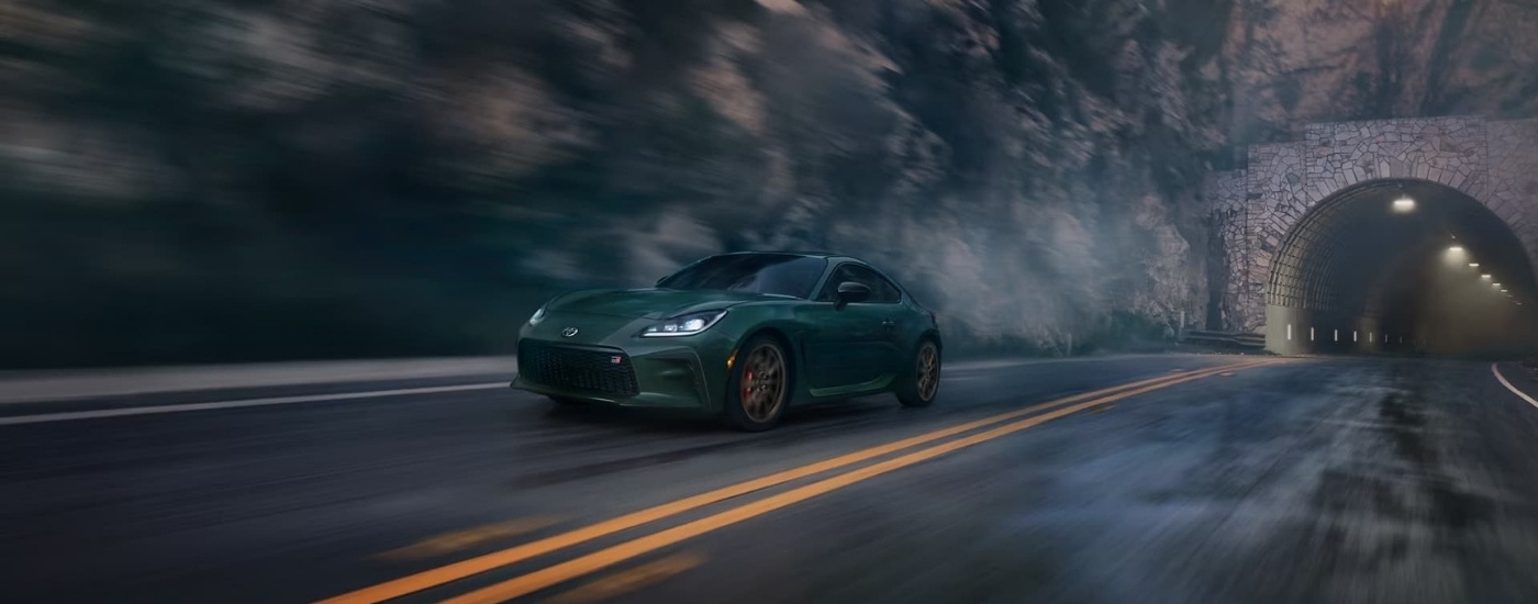 A green 2025 Toyota GR86 Hankone Edition is shown driving to a Toyota dealer near Brattleboro.