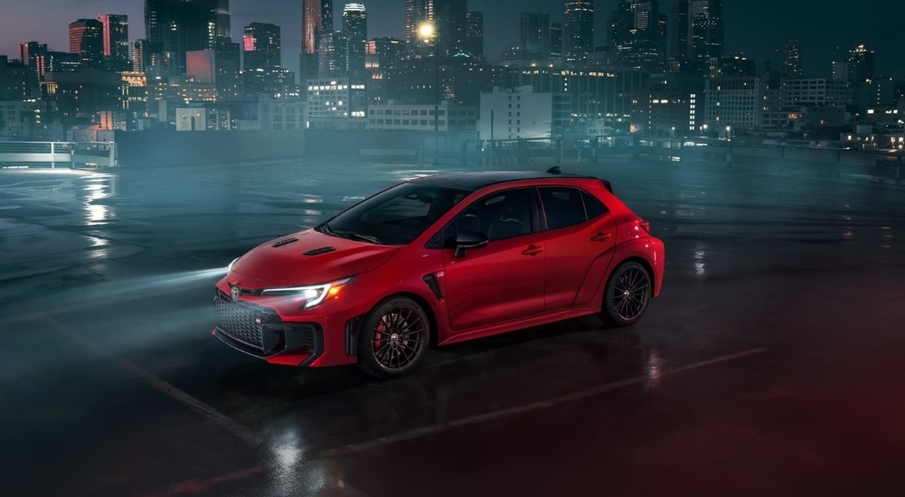 A red 2025 Toyota GR Corolla is shown parked near a city at night.