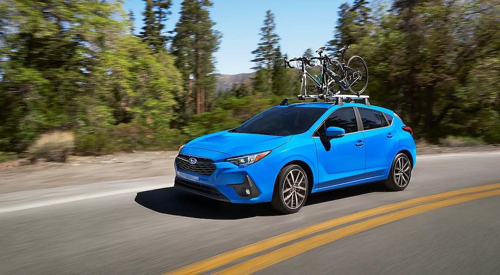 A blue 2024 Subaru Impreza with a mounted bicycle driving around a bend.