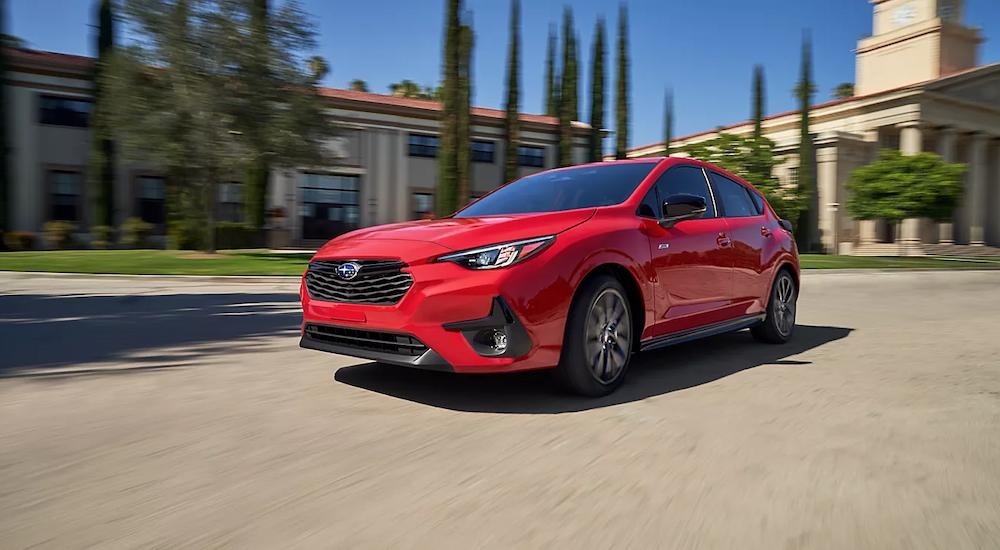 A red 2024 Subaru Impreza driving through a city and facing left.