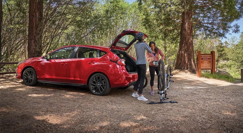 Two people unloading a bicycle from the hatchback of a red 2024 Subaru Impreza RS.