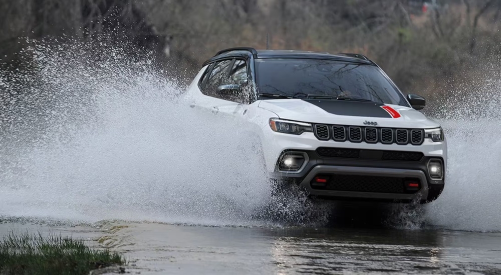 A white 2024 Jeep Compass Trailhawk, purchased from a used Jeep dealer near Poughkeepsie, splashing through water while off-roading.