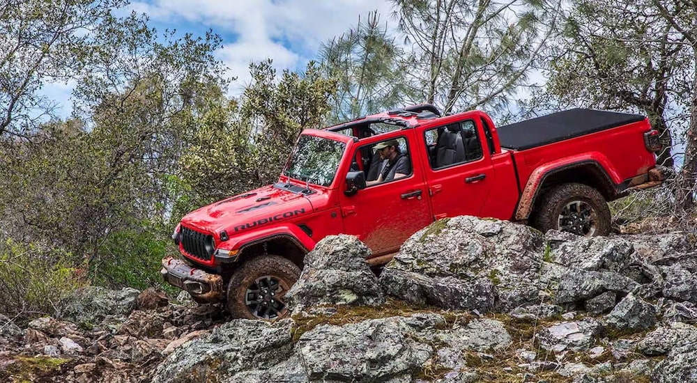 A red 2024 Jeep Gladiator Rubicon off-roading over large rocks.