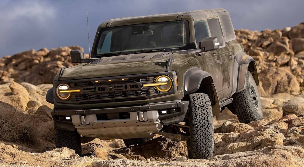 A dark green 2024 Ford Bronco Raptor driving over rocks in a desert.