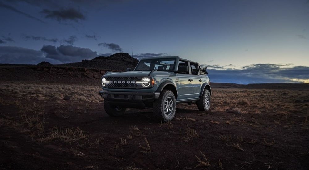 A blue 2024 Ford Bronco Badlands parked off-road on a field and angled left.