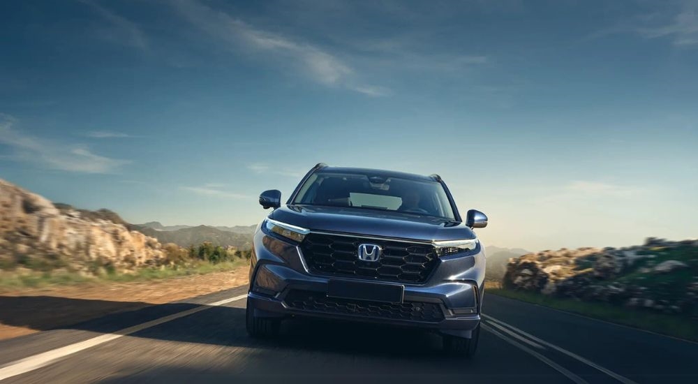 A blue 2025 Honda CR-V Hybrid is shown driving on an open road.