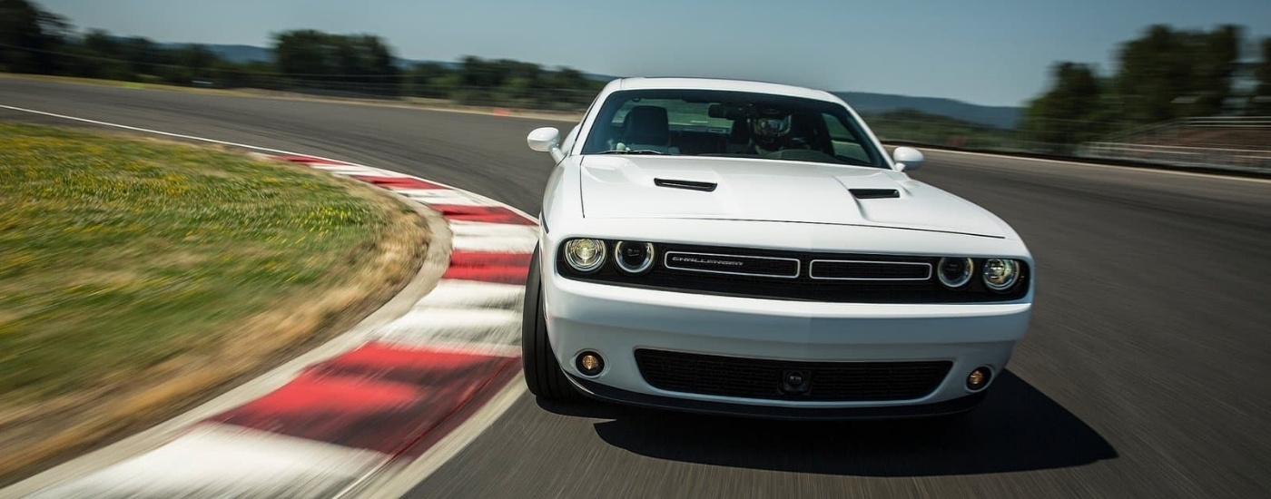 A white 2015 Dodge Challenger is shown rounding a corner on a racetrack.