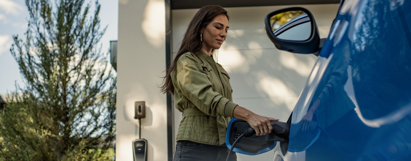 A person is shown charging a blue 2024 Ford Mustang Mach-E for sale near Keene.