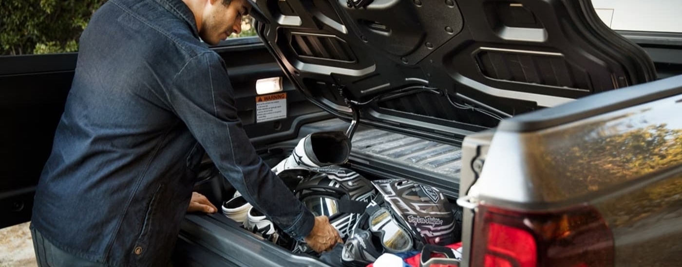 A person is shown stowing gear in the bed of a silver 2023 Honda Ridgeline RTL-E.