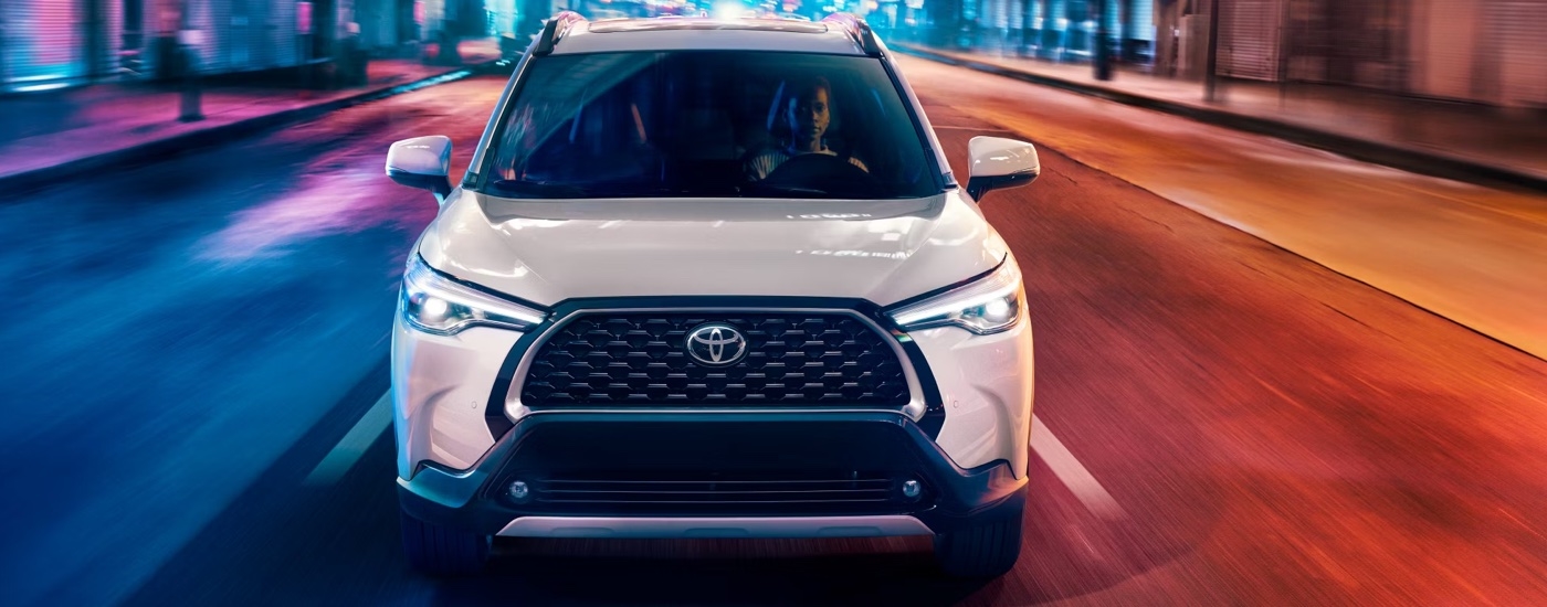 Head-on view of a white 2024 Toyota Corolla Cross XLE driving to a Toyota dealer.