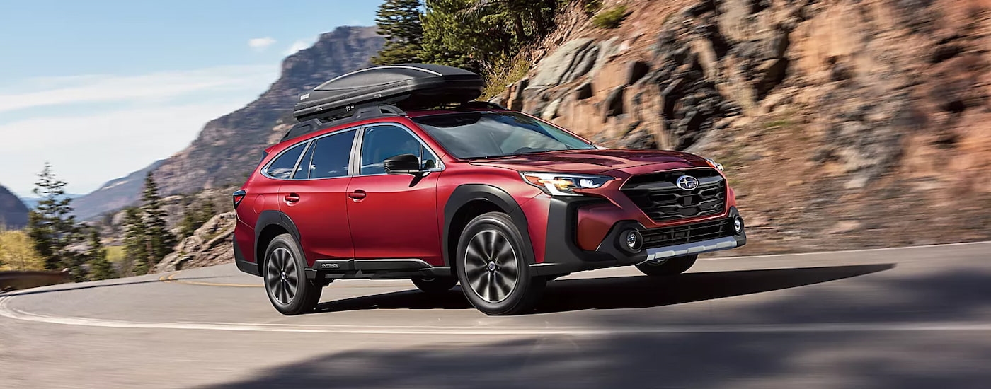 A red 2024 Subaru Outback Limited with a gear box on the roof driving on the highway.