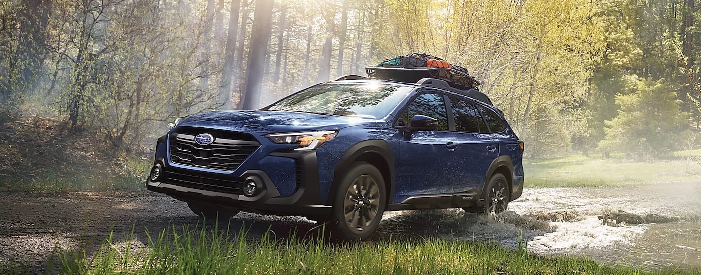 A blue 2024 Subaru Outback Onyx Edition XT off-roading through the woods.