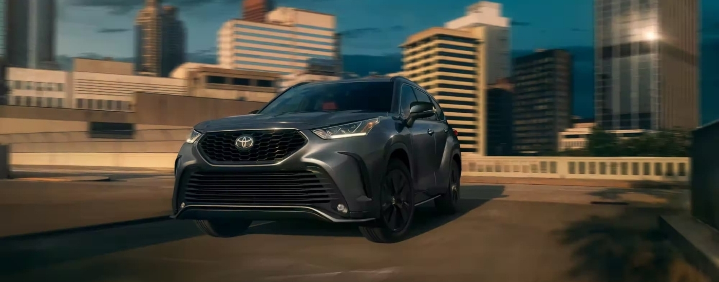 A grey 2024 Toyota Highlander XSE is shown driving past city buildings.