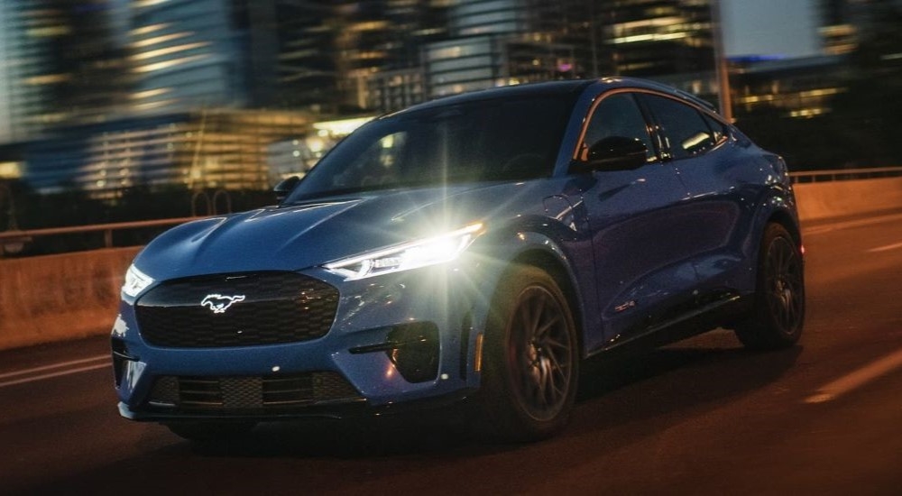 A blue 2024 Ford Mustang Mach-E driving on the highway at night.