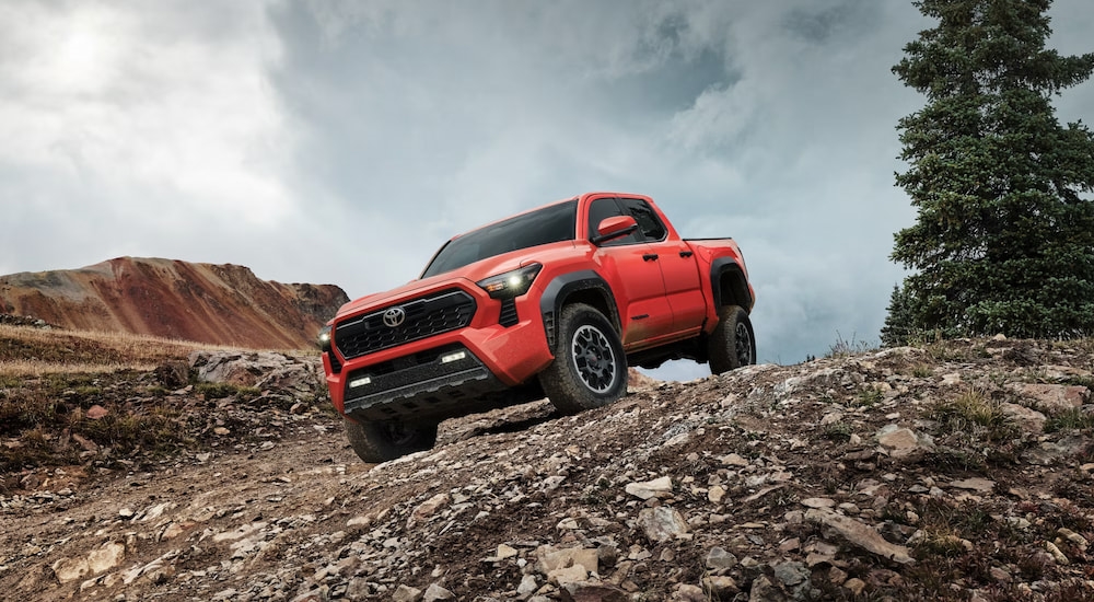 An orange 2024 Toyota Tacoma TRD Off Road driving downhill on a rocky trail.