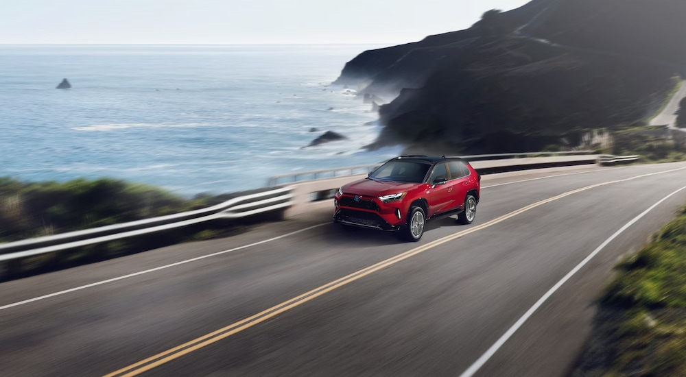 A red 2025 Toyota RAV4 XSE PHEV driving along a coastal road.