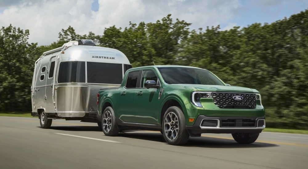 A green 2025 Ford Maverick for sale is shown towing an Airstream.