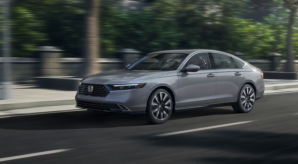 A silver 2025 Honda Accord Touring Hybrid driving on a city street.