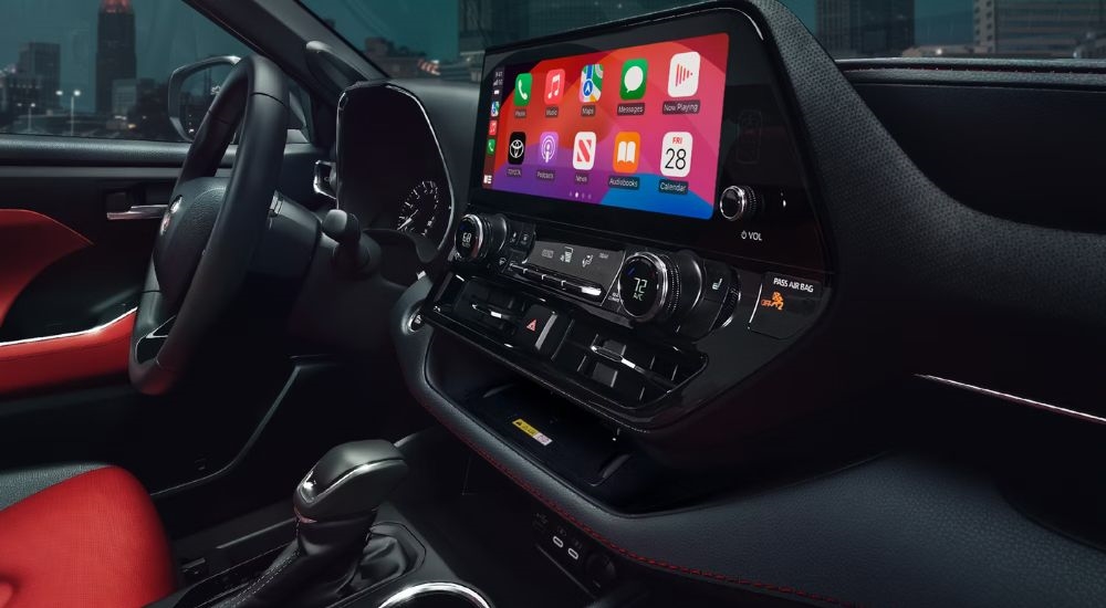 Side angle view of a black and red interior cabin and steering wheel of a 2024 Toyota Highlander XSE.