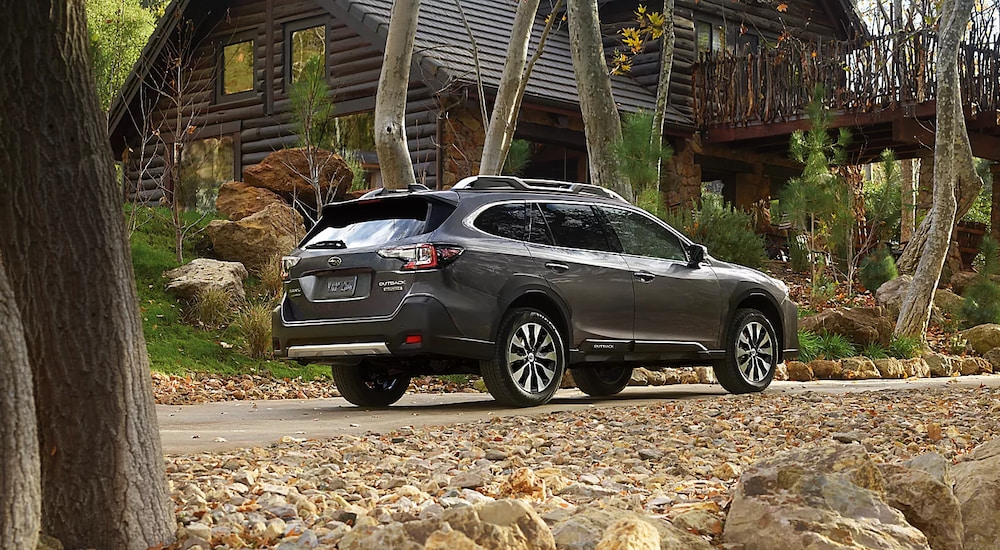 Rear view of a silver 2025 Subaru Outback Touring parked at a cabin in the forest.