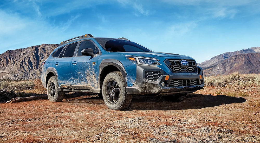 A blue 2025 Subaru Outback Wilderness, splattered with mud from off-roading, parked in the mountains.