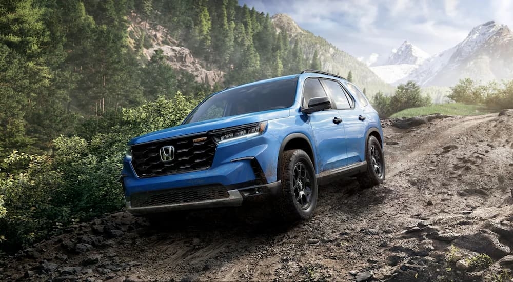 A blue 2023 Honda Pilot driving down a dirt road.