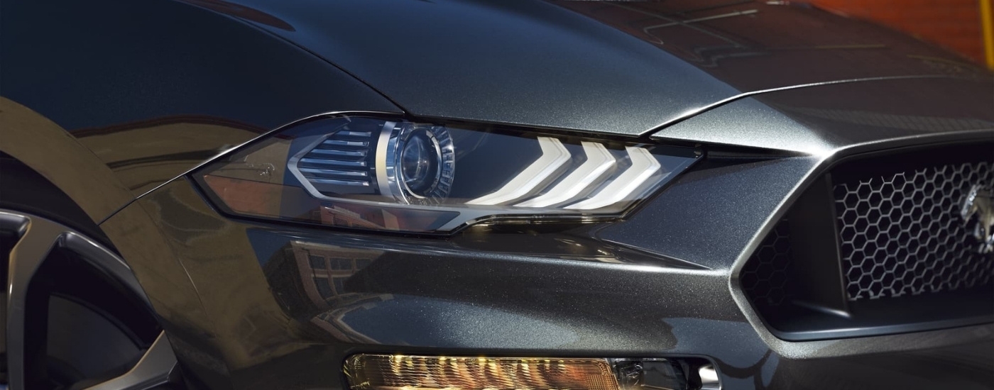 A close-up shows the passenger side headlight on a grey 2020 Ford Mustang.