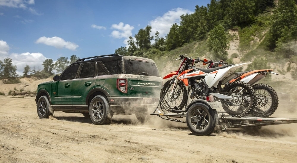 A green 2021 Ford Bronco Sport Badlands is shown towing dirtbikes off-road.