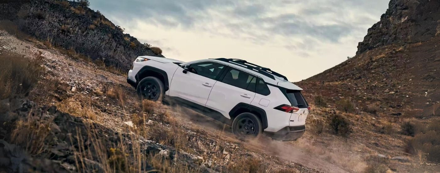 Side angle view of a white 2023 Toyota RAV4 TRD driving off-road up a mountain.