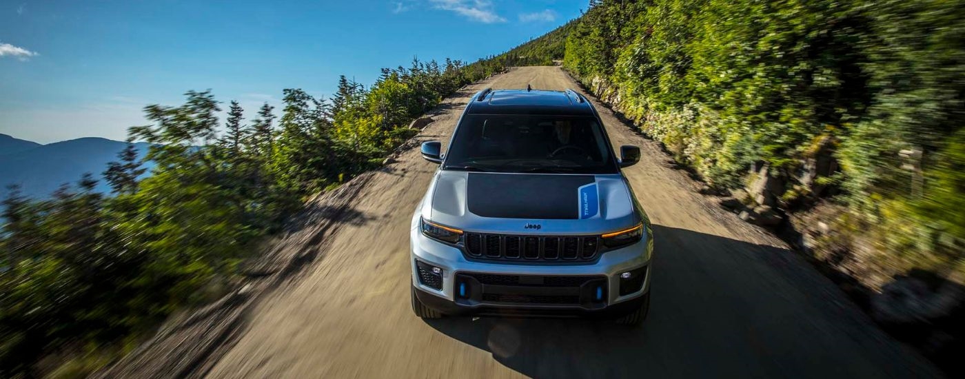 Front view of a white and black 2024 Jeep Grand Cherokee 4xe Trailhawk driving on a dirt road.