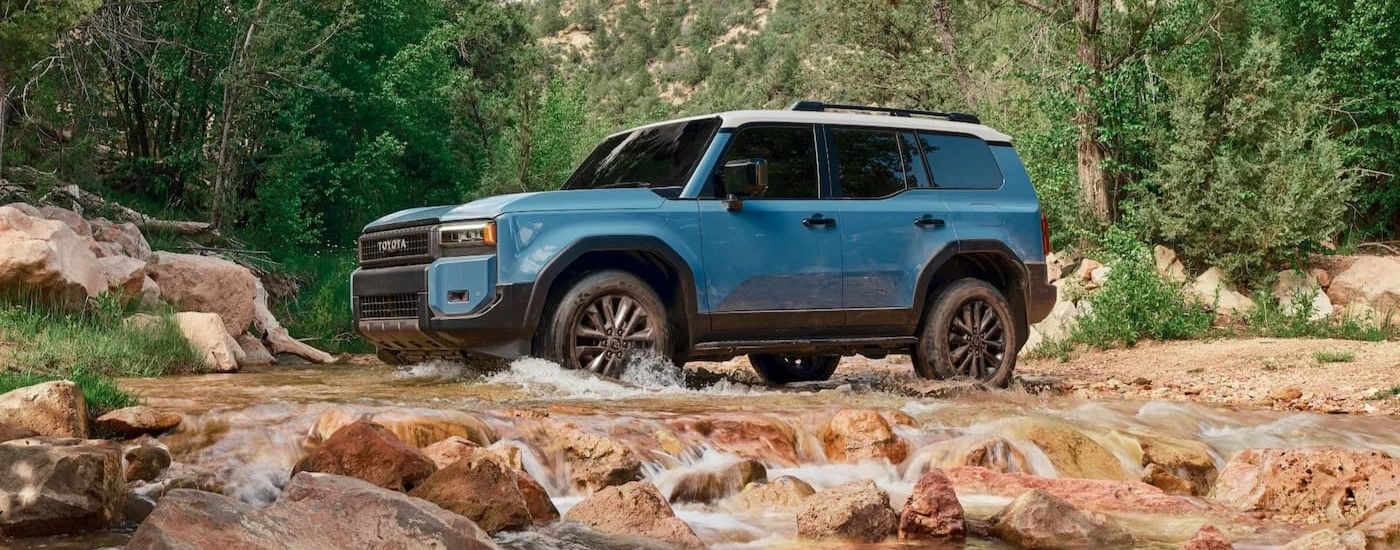 A blue 2025 Toyota Land Cruiser is shown driving through water.