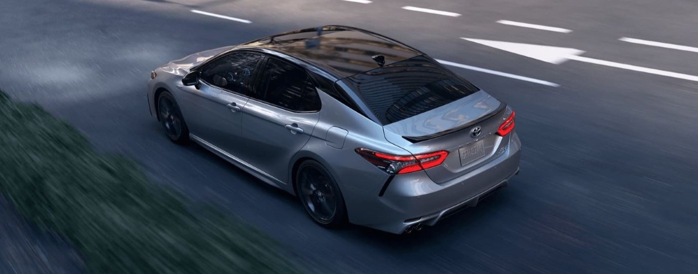 High rear angle view of a grey 2023 Toyota Camry Hybrid driving.