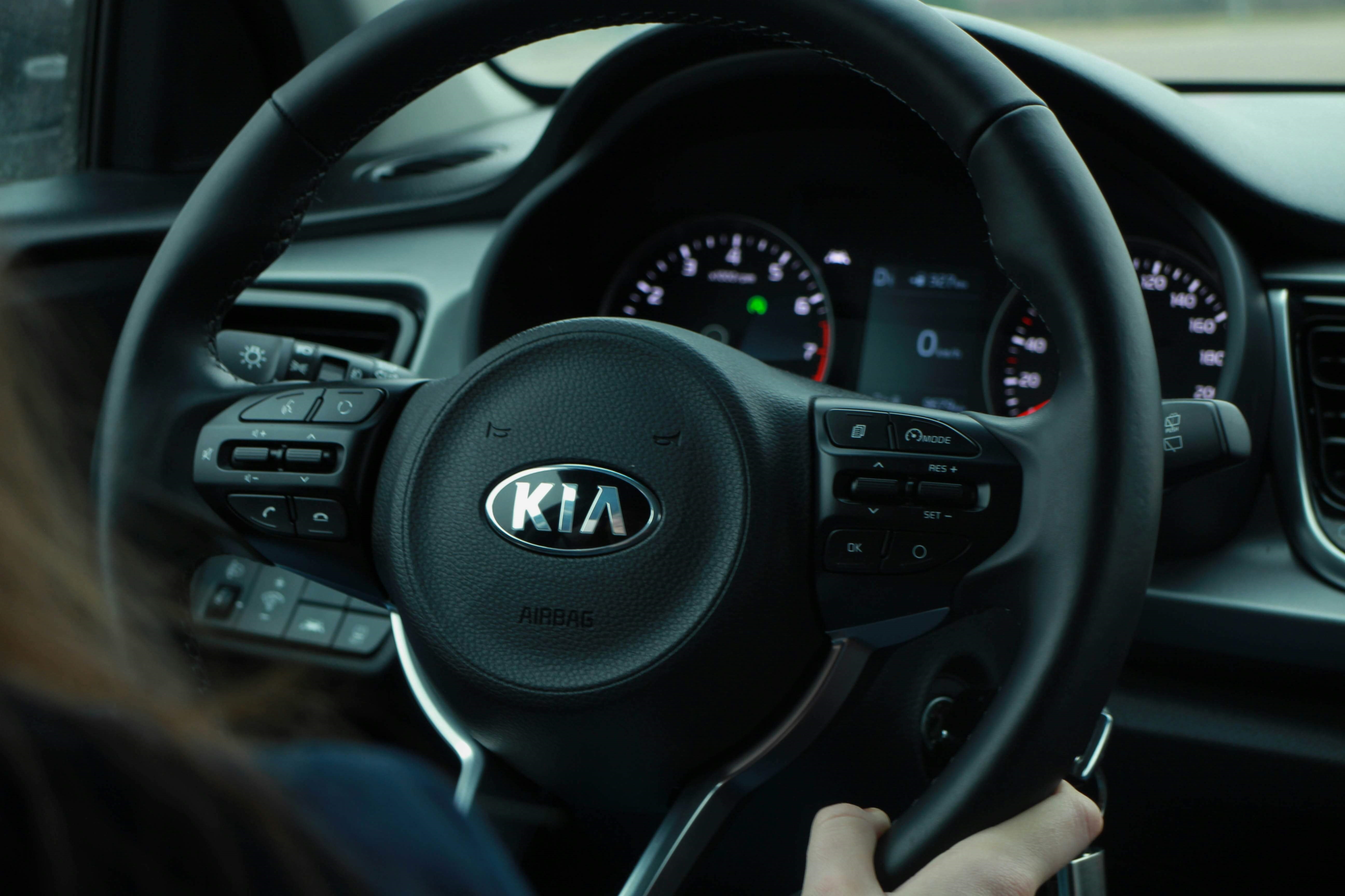 A closeup of a Kia branded steering wheel and dashboard.