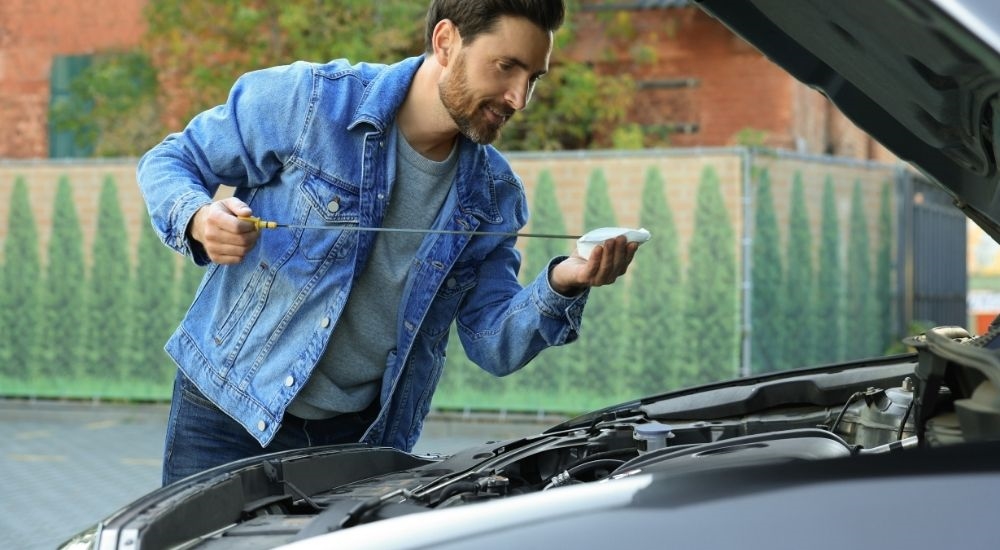 A man bending over the engine of his car as he checks the oil level with a dipstick.