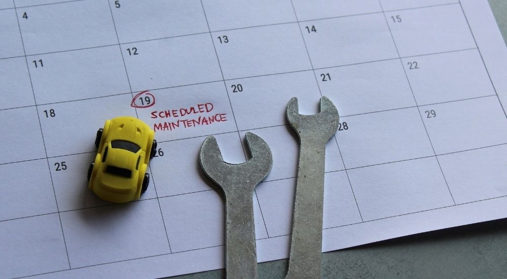 Wrenches and a toy car sitting on a calendar with a Scheduled Maintenance appointment in red.