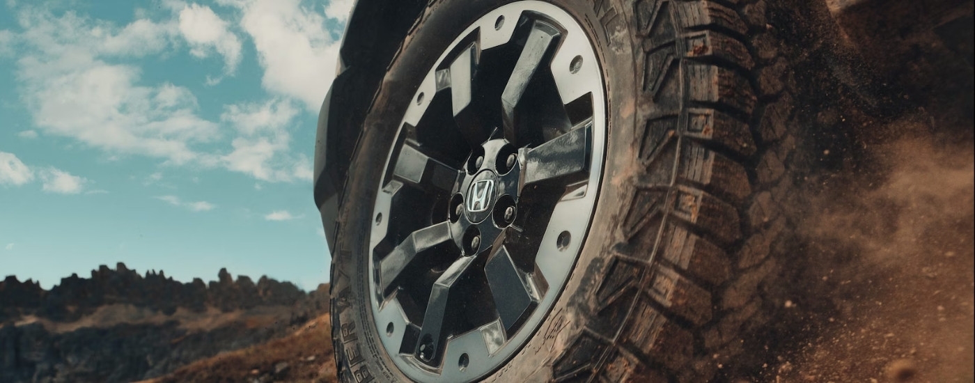 A close-up shows the silver and black wheel on a 2026 Honda Passport Elite Trailsport.