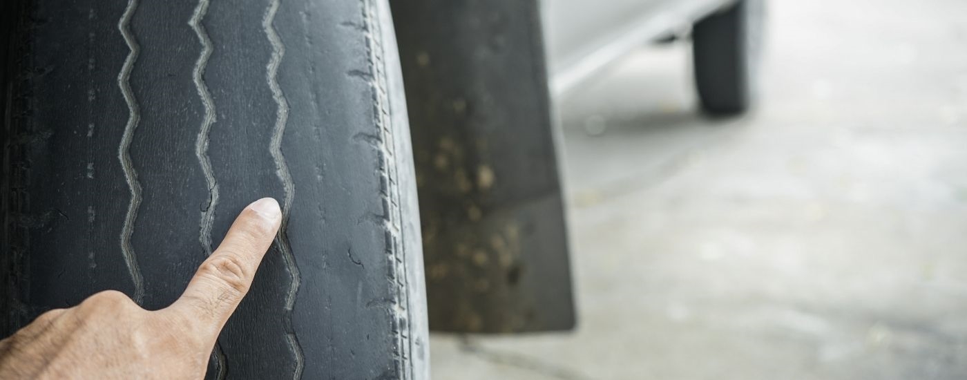 Close-up of a mechanic pointing out unevenly worn tire tread.