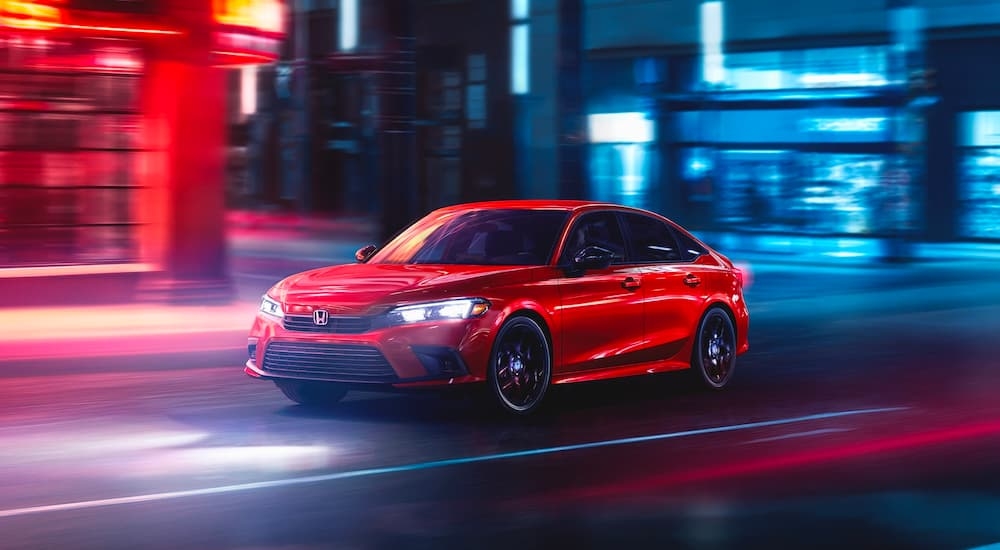 A popular used Honda for sale near North Bergen, a red 2023 Honda Civic Sport, is shown driving on a city street at night.