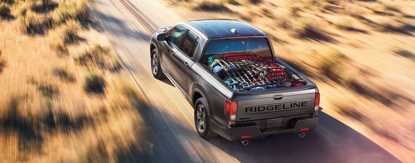 Rear view of a grey 2025 Honda Ridgeline RTL driving down a desert road.