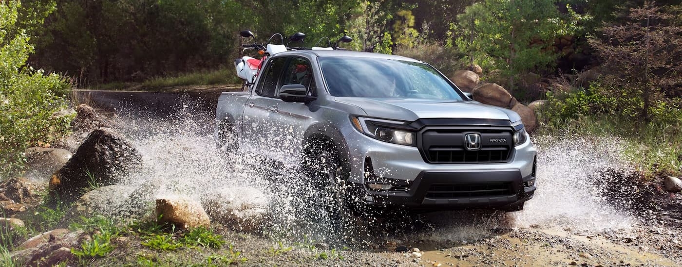 A grey 2025 Honda Ridgeline Sport driving over a shallow river.