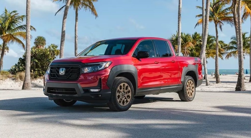 A red 2025 Honda Ridgeline HPD parked near a beach.