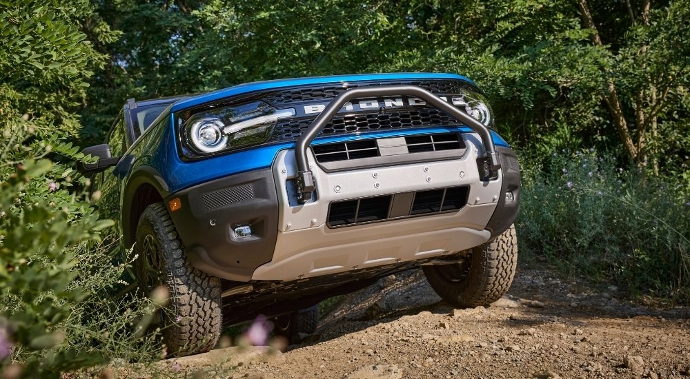 The front end of a blue 2025 Ford Bronco Sport Badlands Sasquatch emerging from trees while off-roading.