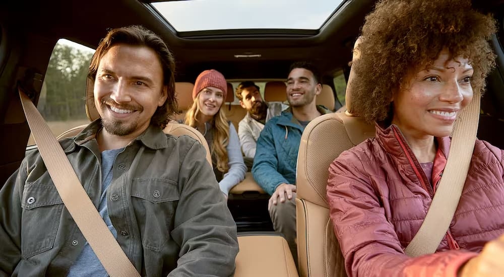 A group of friends are driving in a 2025 Jeep Grand Cherokee L past a Jeep dealer near Hyde Park.