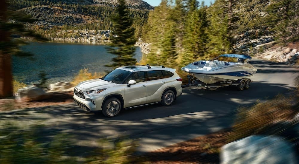 A white 2020 Toyota Highlander towing a boat past a lake.