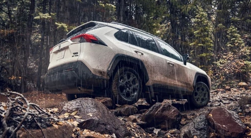 Rear view of a white 2022 Toyota RAV4 TRD off-roading on a muddy trail in the rain.