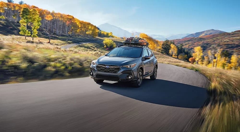 A blue 2024 Subaru Crosstrek is shown driving on a back road.