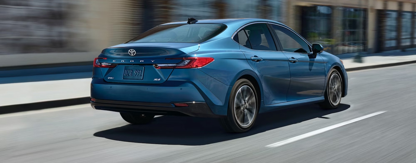 Rear view of a blue 2025 Toyota Camry XLE Hybrid driving to a Toyota dealer near Rutland.